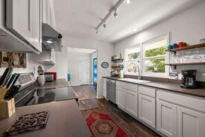 A modern kitchen with white cabinets, a black countertop, and a red patterned rug. - Scenic Bluebird House with Mountain views, AC & Ho (Columbia Falls)