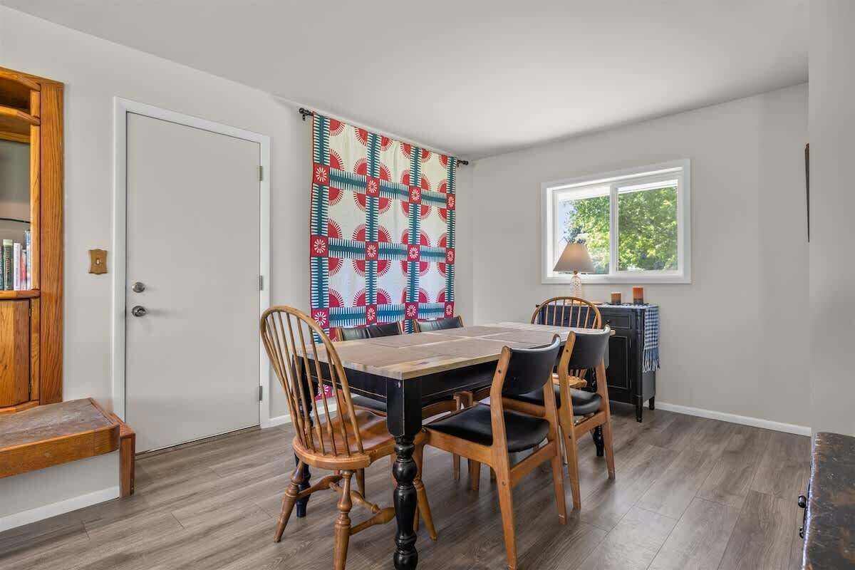 Un comedor con una mesa y sillas de madera, una cortina estampada, un ventanal con vistas y una estantería.