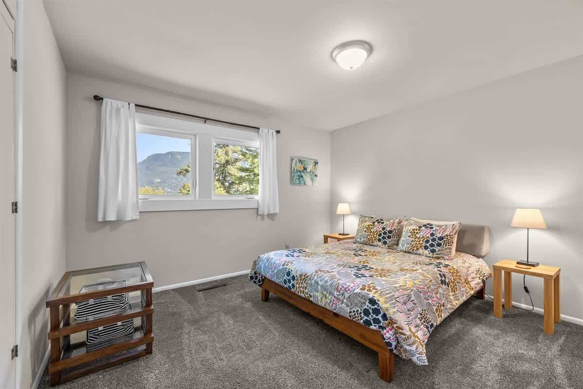 A bedroom with a bed, two bedside tables, a window with curtains, a lamp on each table, and a small table with magazines.