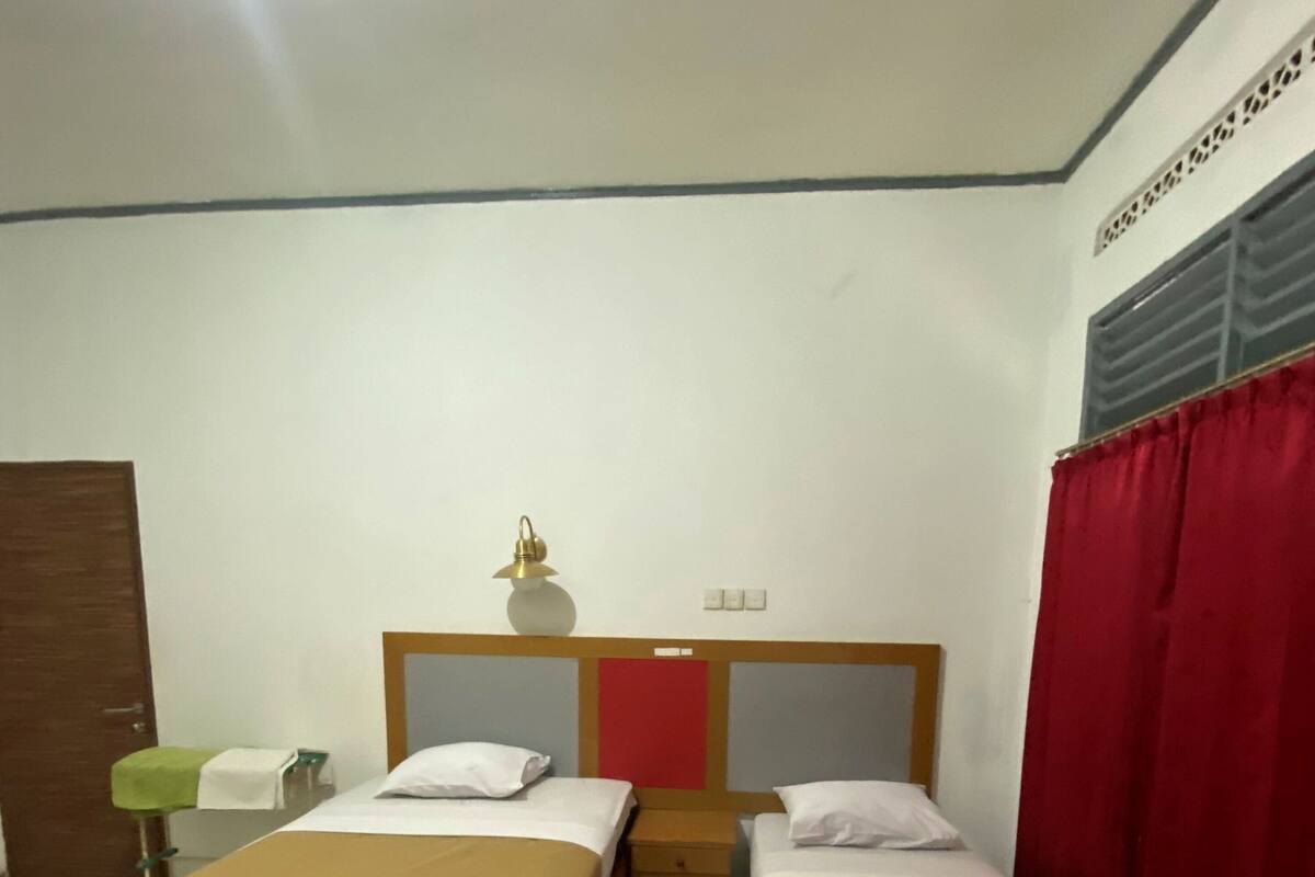 A room with two single beds, a nightstand, a lamp, and a red curtain.