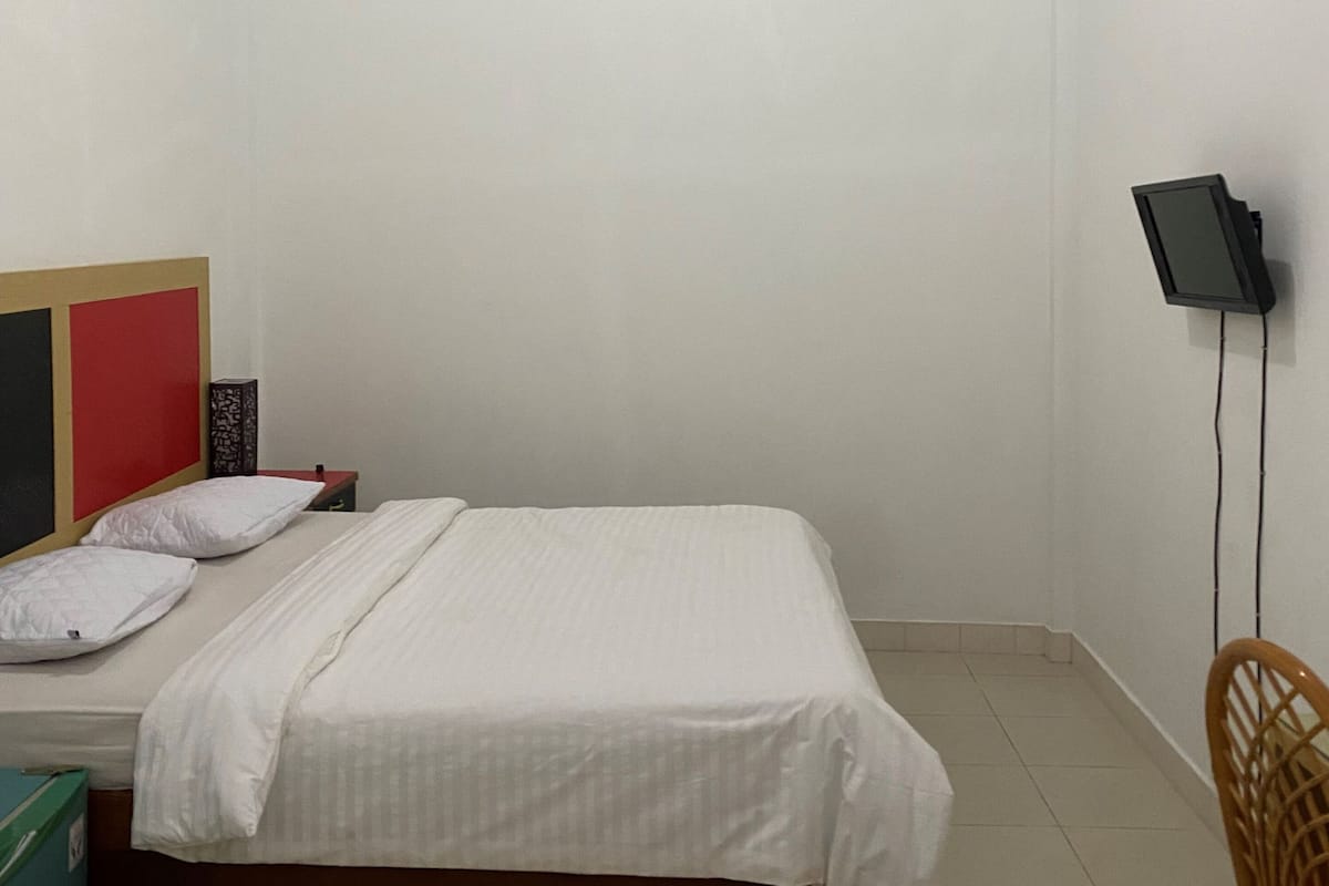 A bedroom with a bed, a TV mounted on the wall, and a chair.