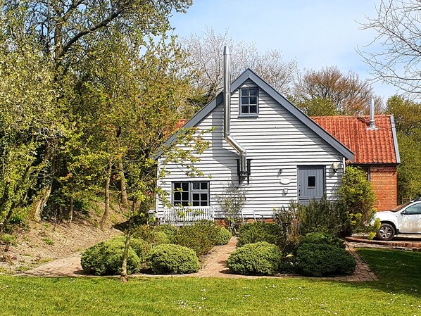 Une maison blanche avec un toit rouge, entourée de verdure et dotée d’une allée pavée.