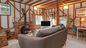 A cozy living room with exposed wooden beams, a fireplace, a sofa, a TV, and a table with a lamp. - Twosome (Halesworth)