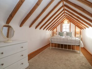 Une chambre avec un plafond en pente, un lit, une commode et un miroir.