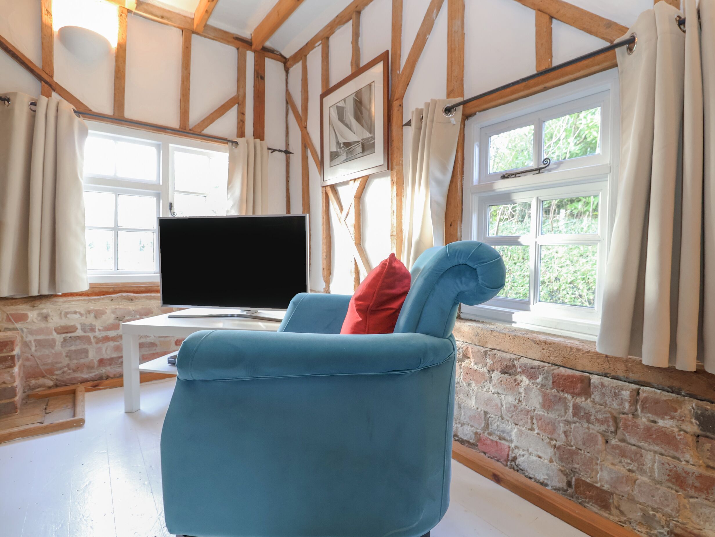 En stue med en blå sofa, et fladskærms-tv på et hvidt bord og en murstensvæg.