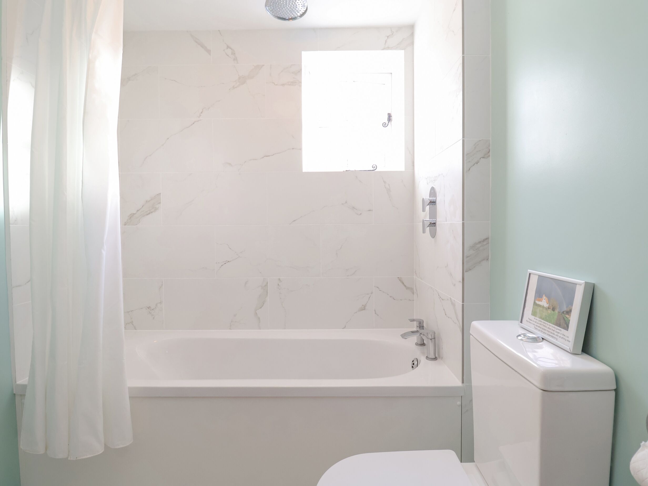 A bathroom with a bathtub, toilet, and a framed picture on the wall.