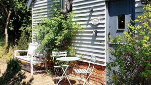 A rustic cabin with a porch, a small table, and two chairs. - Twosome (Halesworth)