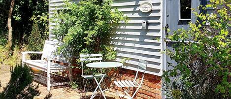 A rustic cabin with a porch, a small table, and two chairs.