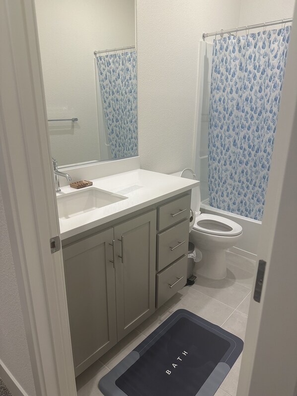 Une salle de bain avec un lavabo blanc, un miroir et des toilettes. Il y a un rideau de douche avec un motif bleu.