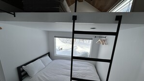 A compact room with a bunk bed, a small window with a view of a snowy landscape, and a wooden hanger rack.