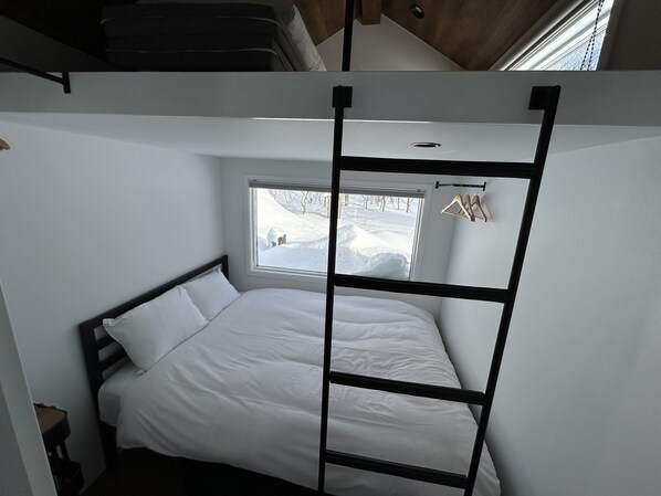 A compact room with a bunk bed, a small window with a view of a snowy landscape, and a wooden hanger rack. - EL CAMINO Makkari (Makkari-mura)