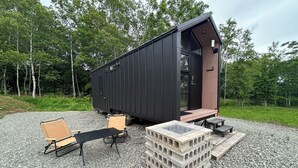 A modern, dark-colored cabin with a wooden deck and a small outdoor seating area.