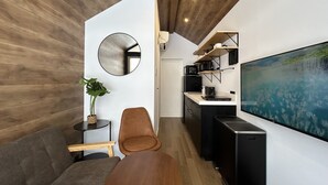 A modern living space with a wooden ceiling, a round mirror, a sofa, a coffee table, a TV, and a kitchen area with a large window.