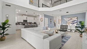 A modern, open-plan living area with a sectional sofa, dining table, and kitchen in the background. - Precious Villa 5Beds/4Baths/Pool/18Min Disney (Davenport)