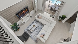 A modern living room with a white sofa, a coffee table, and a flat-screen TV mounted on a wooden wall. There is a staircase leading to an upper level, and a view of a swimming pool through large windows. - Precious Villa 5Beds/4Baths/Pool/18Min Disney (Davenport)