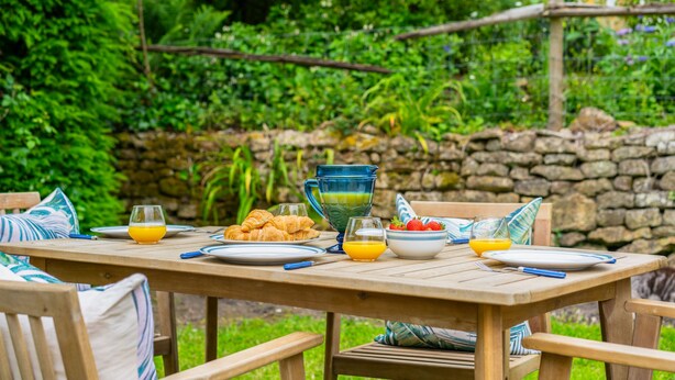 Ein Holztisch, reich gedeckt mit Frühstücksleckereien wie Croissants, Orangensaft und Erdbeeren.