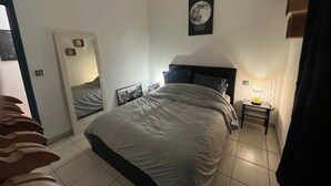 A bedroom with a bed, a bedside table with a lamp, a mirror, and a framed picture on the wall.