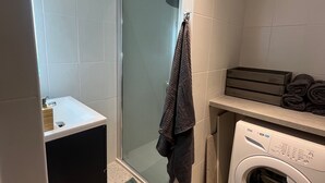 A modern bathroom with a glass shower enclosure, a sink, a washing machine, and a towel rack.