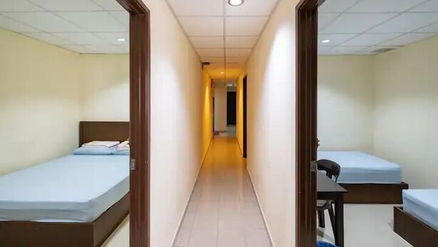 Un pasillo con dos camas individuales a cada lado, un escritorio con una silla y una puerta al final.