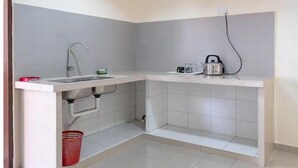 Una pequeña cocina con un lavamanos, un hervidor y una cesta roja.