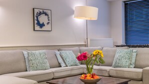 A living room with a beige sofa, a wooden coffee table with a bowl of fruit, and a floor lamp.