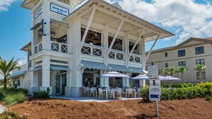A two-story building with a beach service sign, outdoor seating with umbrellas, and a sign for the Chapel Crosspoint. - FREE Golf Cart | New home located on resort style pool | Massive Kitchen/Private Balconies/Sleeps 12 (Santa Rosa Beach)