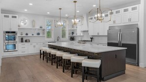 A modern kitchen with white cabinetry, stainless steel appliances, and a central island with bar stools. - FREE Golf Cart | New home located on resort style pool | Massive Kitchen/Private Balconies/Sleeps 12 (Santa Rosa Beach)