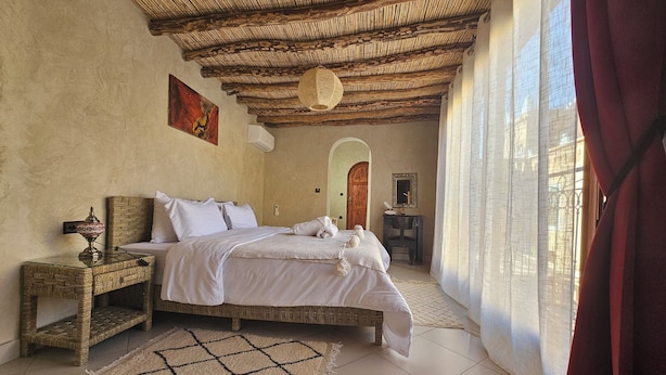 A bedroom with a bed, a nightstand, a mirror, and a door. - Kasbah La Cigogne (Aït Benhaddou)