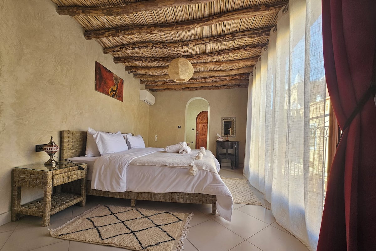 Quarto com uma cama, mesa de cabeceira, espelho e porta.