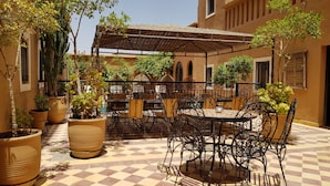 An outdoor patio with checkered flooring, metal tables and chairs, and potted plants. - Kasbah La Cigogne (Aït Benhaddou)
