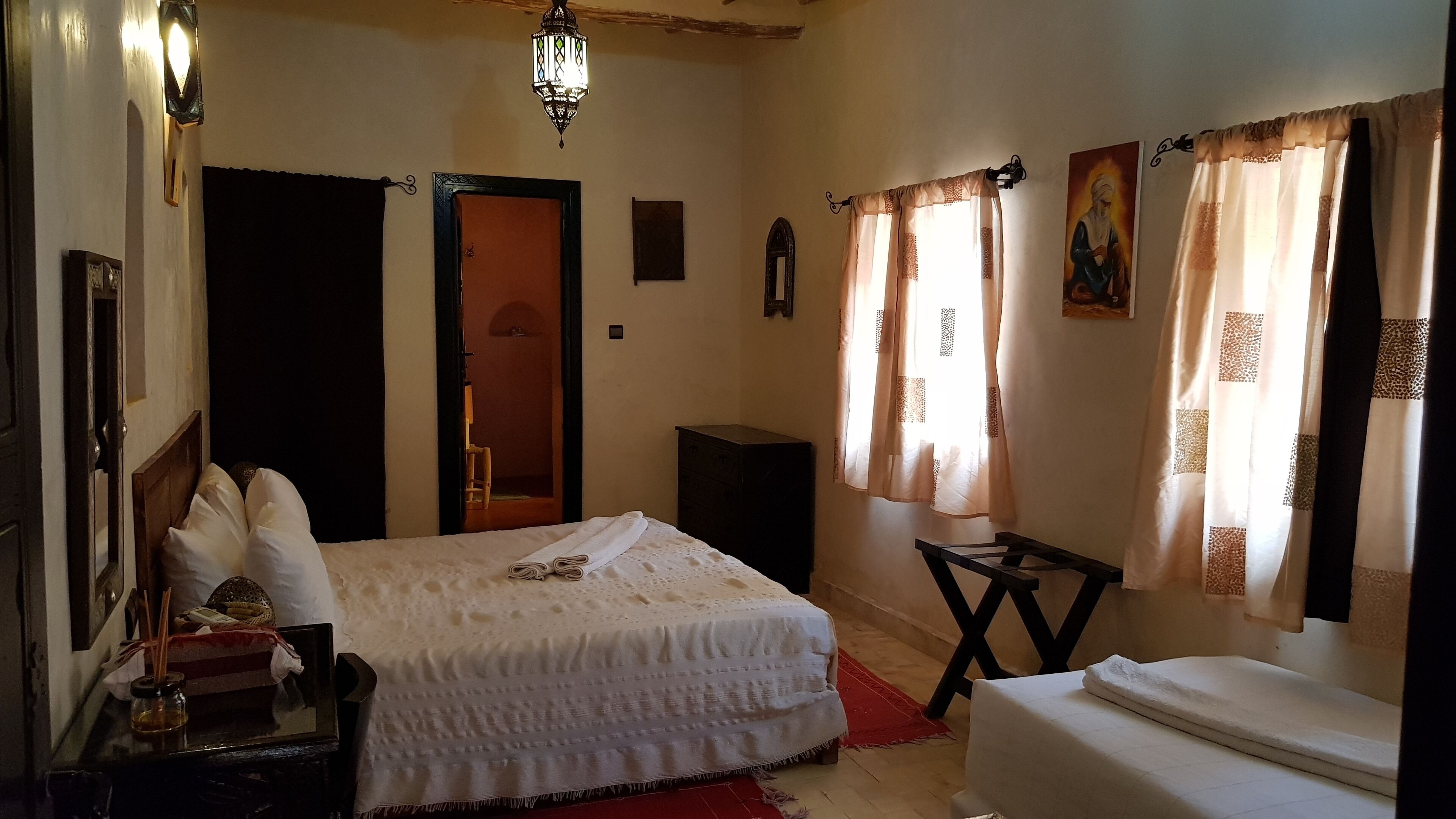 A bedroom with a bed, bedside table, lamp, and a door leading to another room.