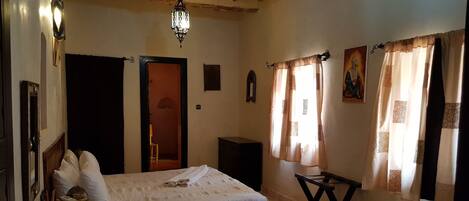 Un dormitorio con cama, mesita de noche, lámpara y una puerta que da a otra habitación.
