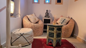 A cozy living area with wicker furniture, a small table with bottles, and a statue. - Kasbah La Cigogne (Aït Benhaddou)