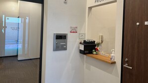 A hotel reception area with a reception desk, a digital keycard reader, a welcome sign, and a wooden shelf with a welcome sign, a bottle of hand sanitizer, and a small decorative item. - KYU KYU HOTEL (Tokyo)