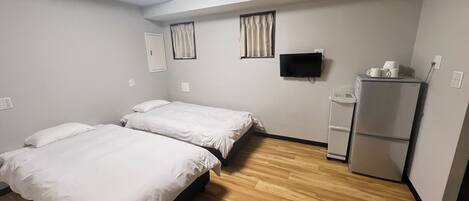 A hotel room with two beds, a flat-screen TV, a refrigerator, and a window with curtains.