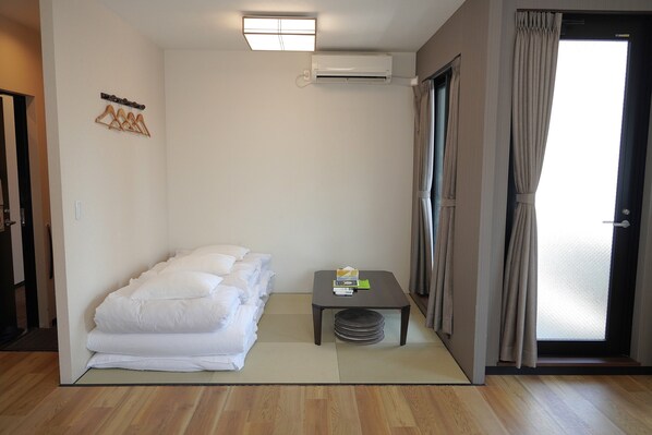 A room with a bed, a small table, a wall-mounted air conditioner, and a sliding door with curtains.