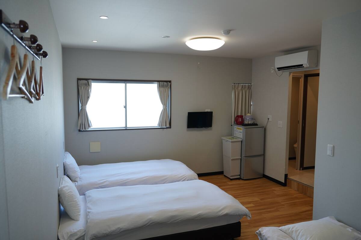 A bedroom with two beds, a television, an air conditioning unit, and a small kitchenette.