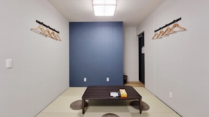A room with a dark wooden table, two tatami mats, a blue accent wall, and wooden hangers on the walls. - KYU KYU HOTEL (Tokyo)