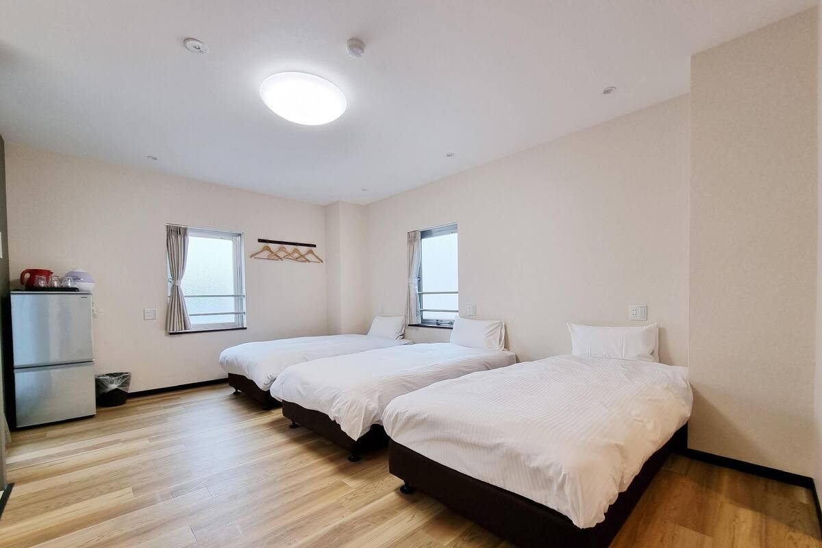 A room with two beds, a small kitchenette, and a ceiling light.