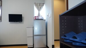 A compact kitchen with a refrigerator, a small countertop, a television mounted on the wall, and a shelf with blue slippers. - KYU KYU HOTEL (Tokyo)