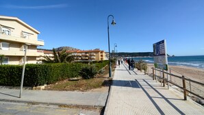 Ein Küstenweg mit befestigtem Gehweg, einer Straßenlaterne und einem Strand im Hintergrund.