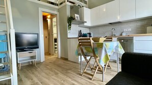 Eine kompakte Küche mit weißen Schränken, ein Essbereich mit Tisch und Stühlen, ein Fernseher und ein Holzboden.