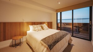 A modern bedroom with a large bed, a wooden headboard, a small side table, and a balcony with a view. - 95 Hardy Street Apartment 4 (Nelson)
