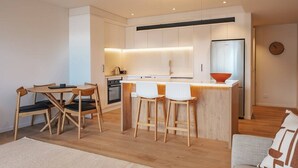 A modern kitchen with a central island, wooden chairs, a dining table, and a sofa. - 95 Hardy Street Apartment 4 (Nelson)