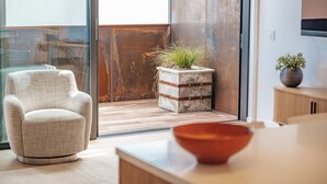 A modern living room with a large window, a white armchair, a small wooden cabinet, and a potted plant. - 95 Hardy Street Apartment 4 (Nelson)