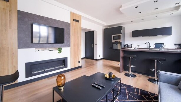 Uma sala de estar moderna com televisão de tela plana, lareira e área de jantar com mesa e cadeiras pretas.