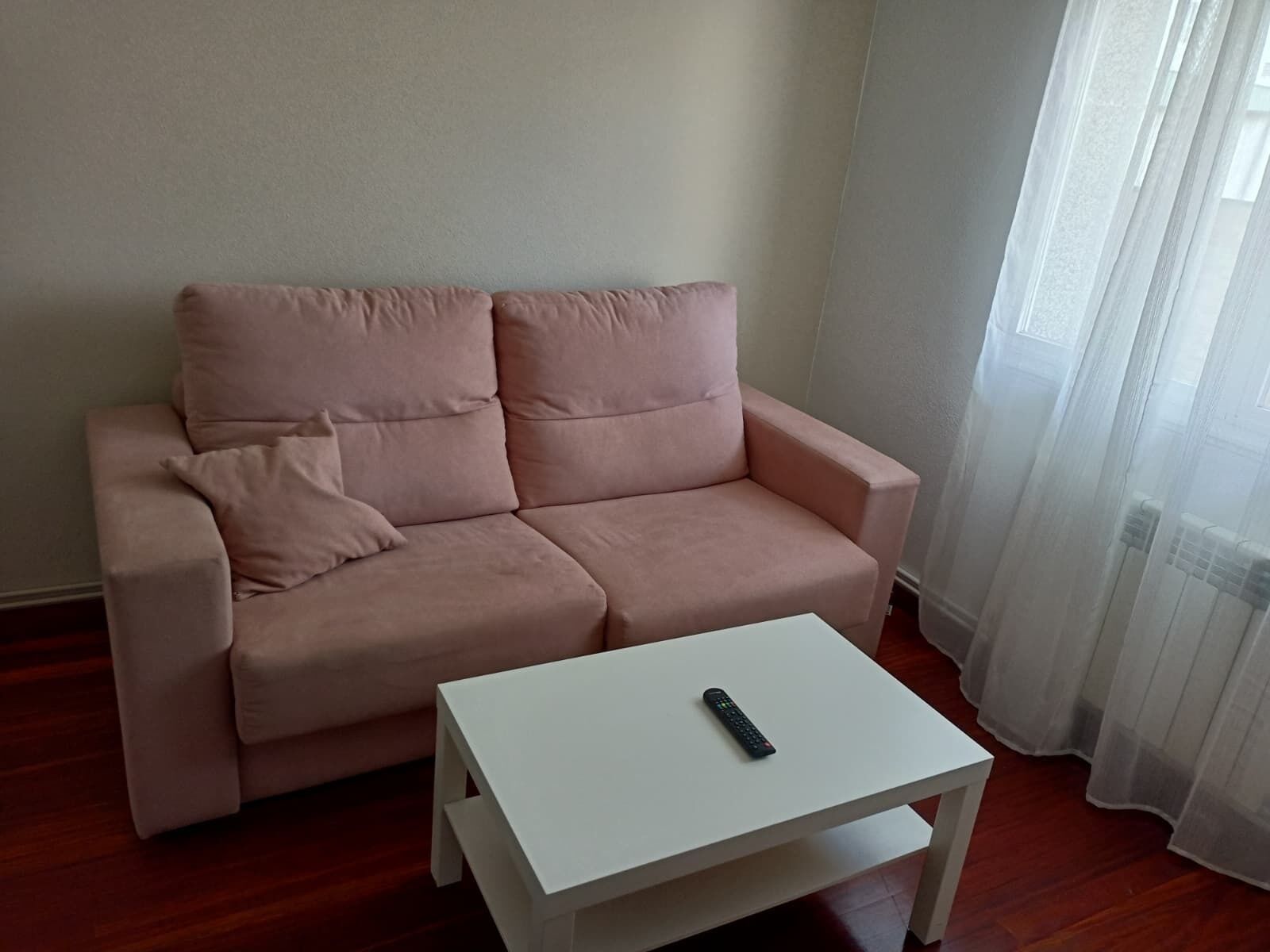 Un sofá rosa con una mesita de centro blanca y un control remoto encima.