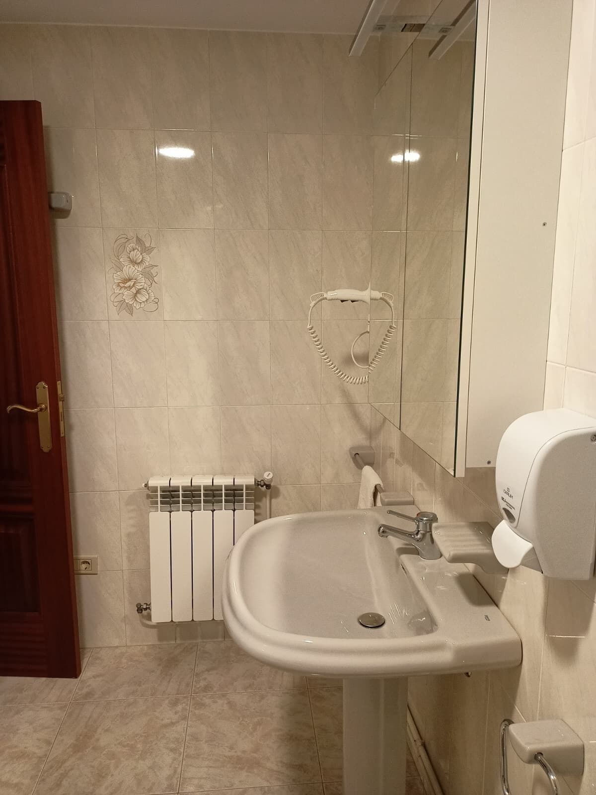Een badkamer met een wit wastafel, een handdoekhouder in de vorm van een hart, een handdroger en een radiator.