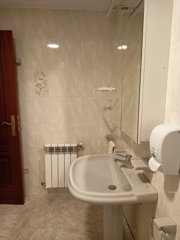 Un baño con un lavabo blanco, un toallero con forma de corazón, un secamanos y un radiador.