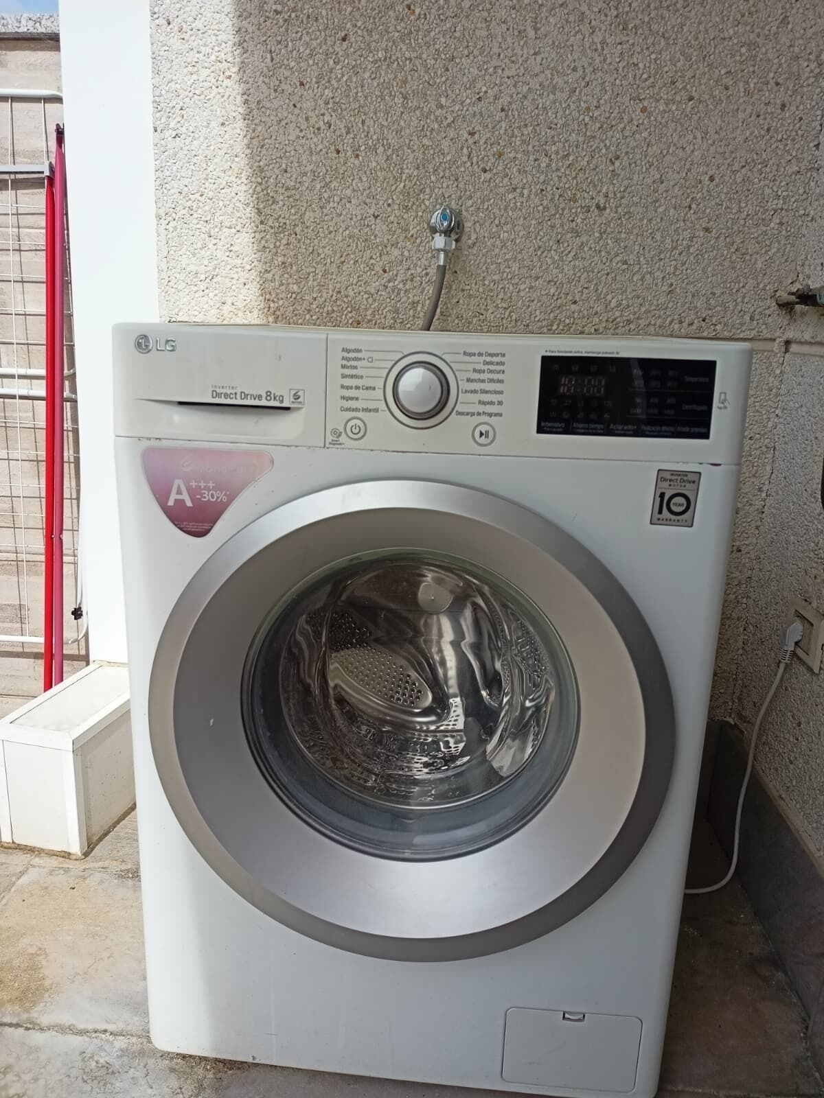Une machine à laver à chargement frontal dotée d’un écran numérique, d ’un tuyau d’arrivée d’eau et d’un panneau de commande avec divers réglages.